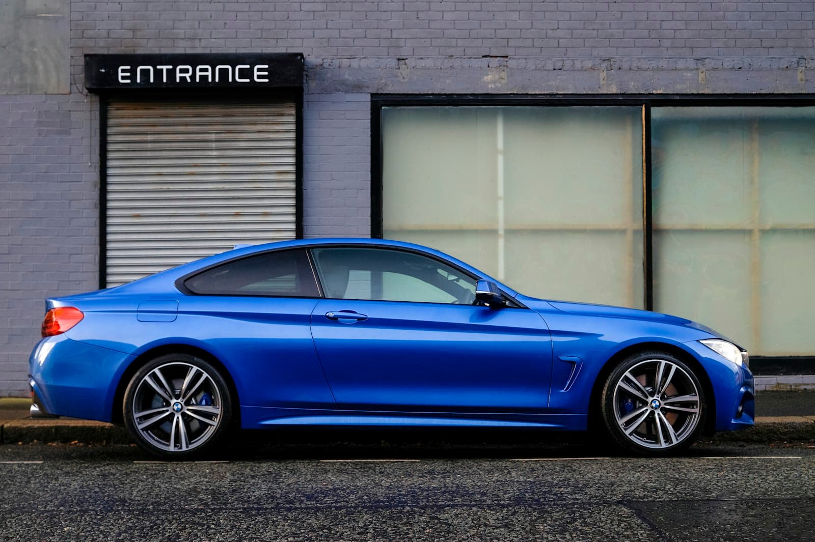 Blue BMW 4 Series coupe parked in profile on a city street