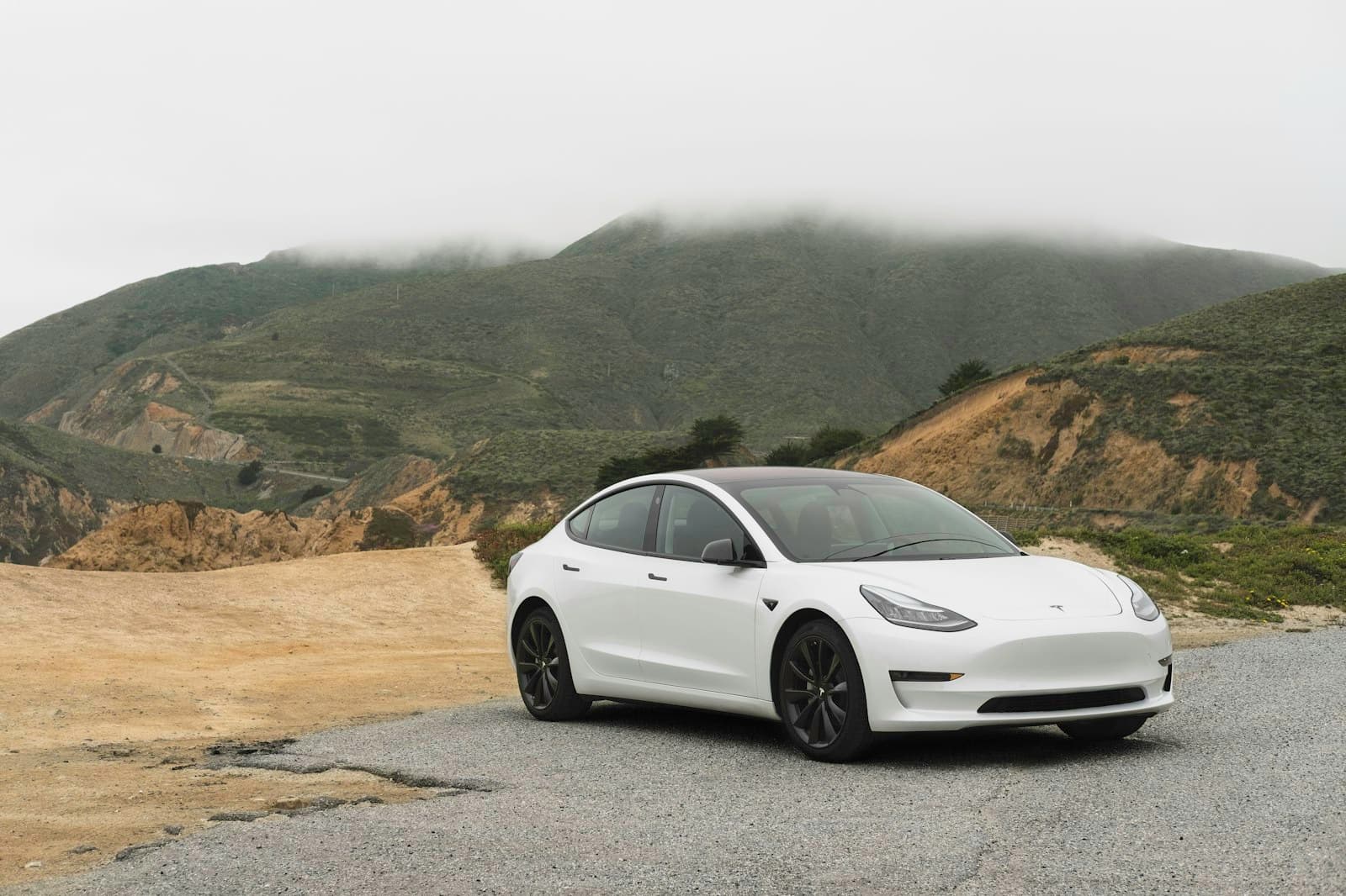 White Tesla Model 3 on a gravel overlook above a foggy coastline